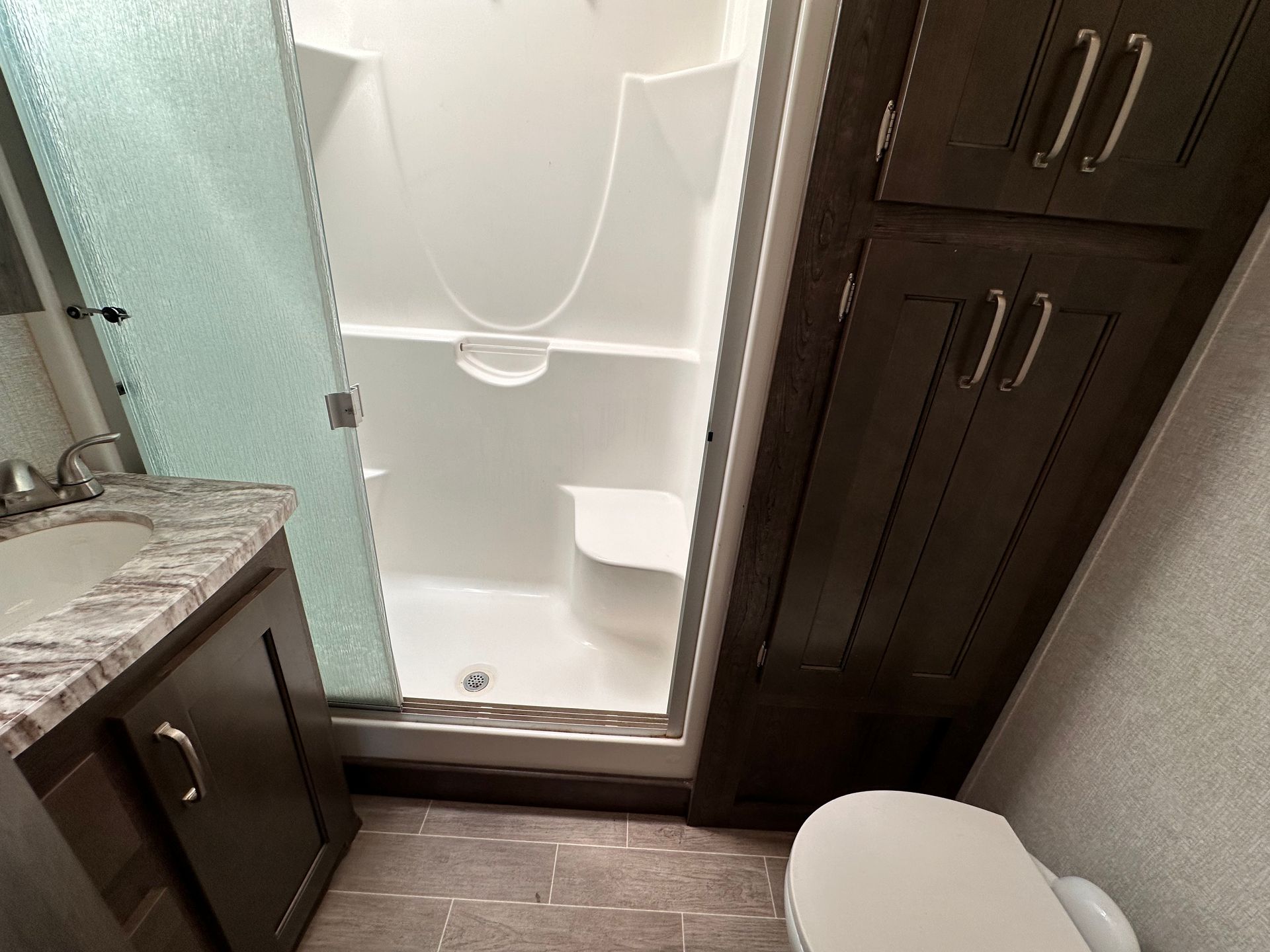 A bathroom with a toilet , sink , shower and cabinets.