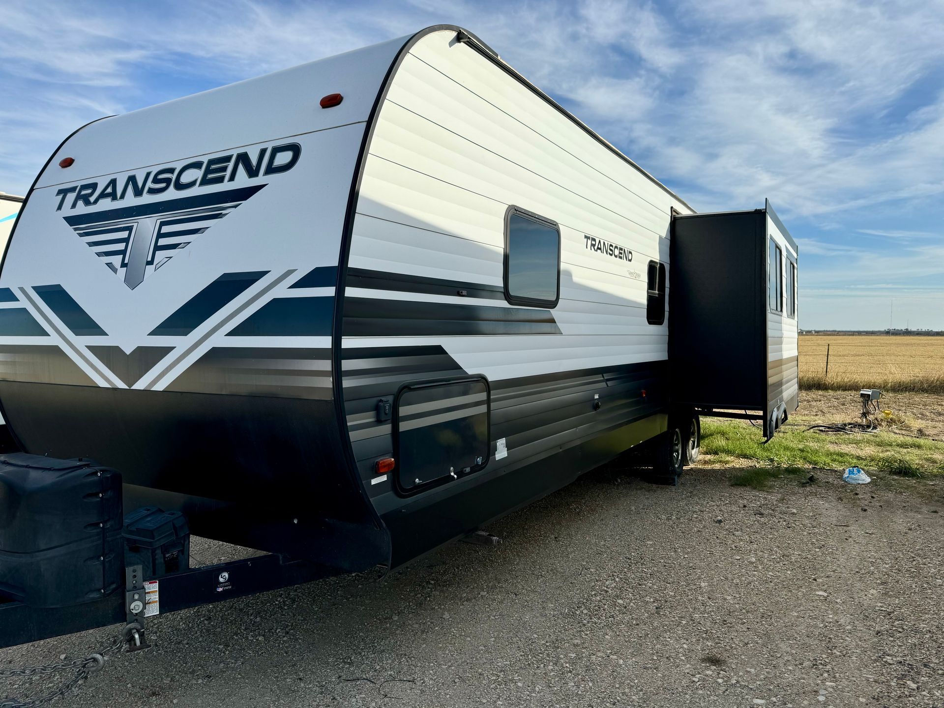 A white and black trailer is parked in a gravel lot.