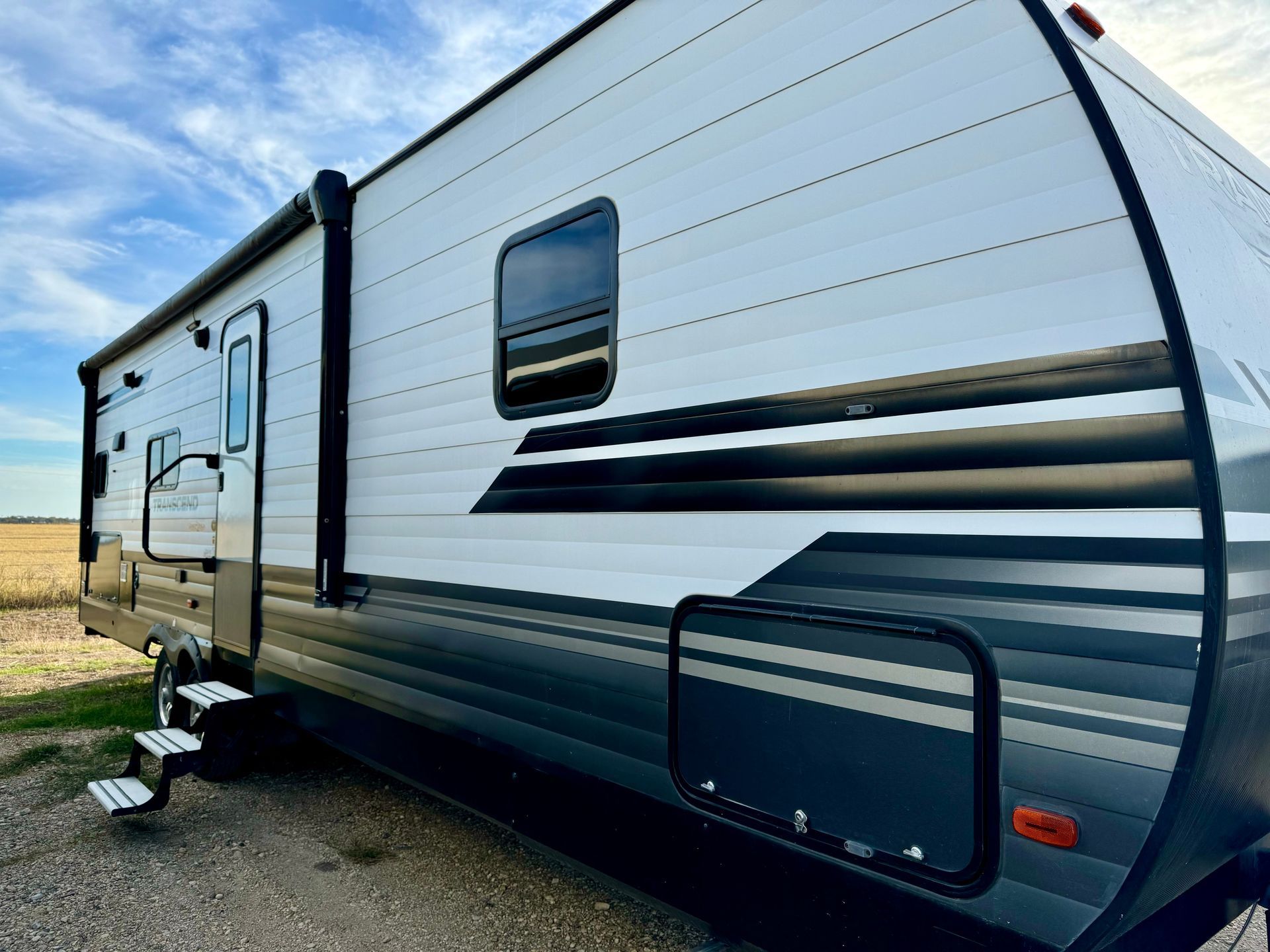 A white and black trailer is parked in a gravel lot.