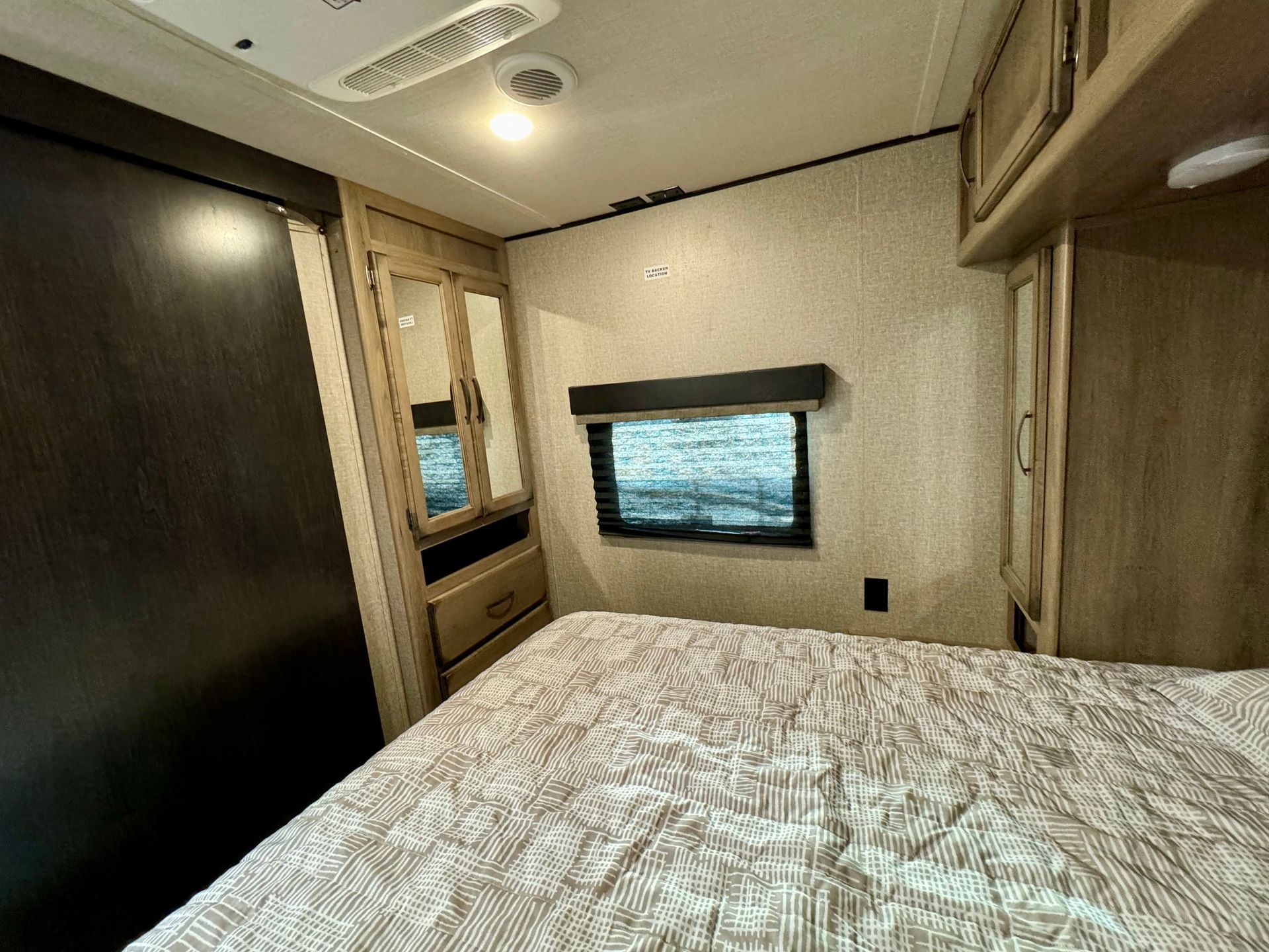 A bedroom in a rv with a bed , dresser , mirror and window.