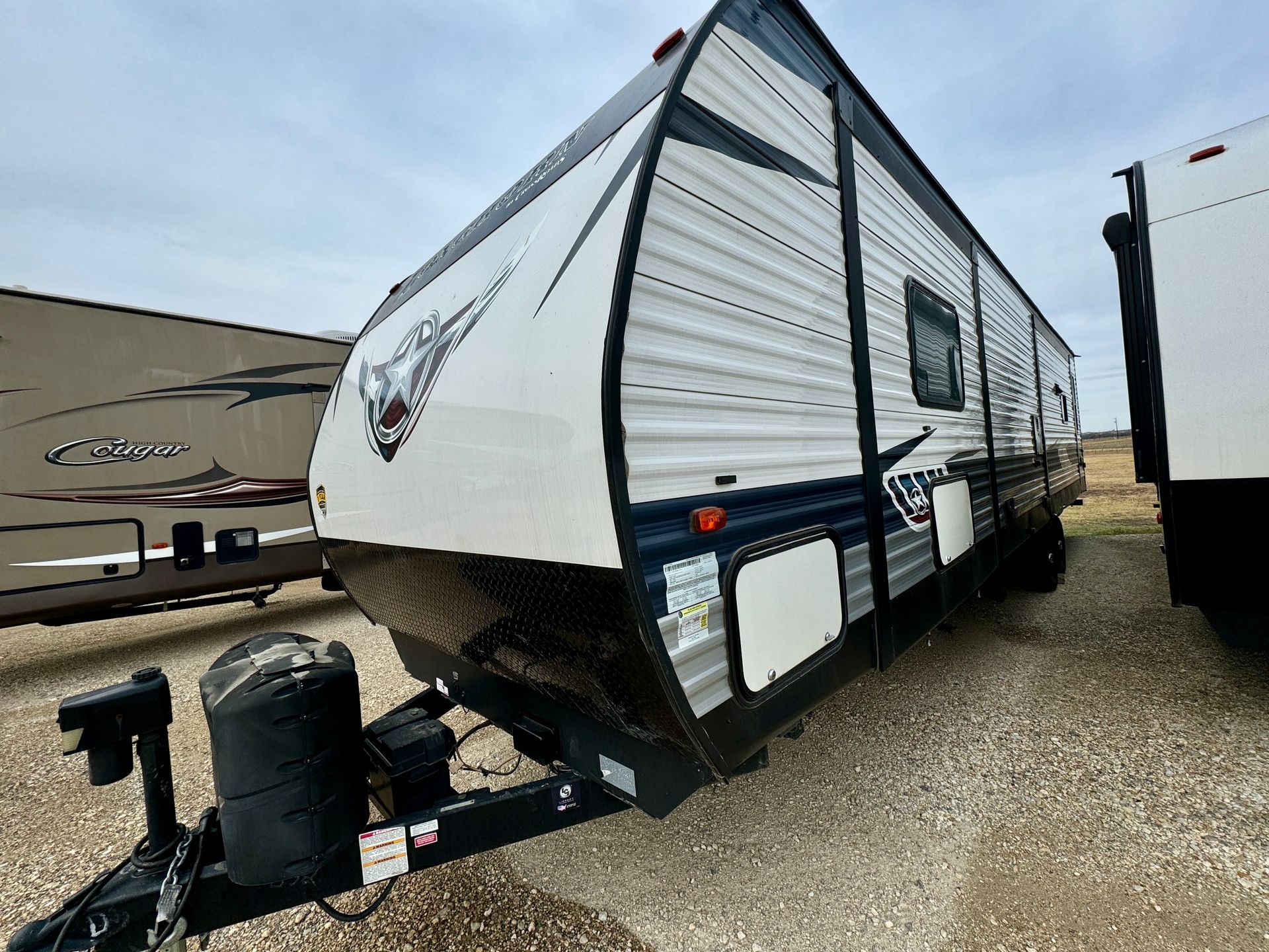 A white and blue trailer is parked in a gravel lot.