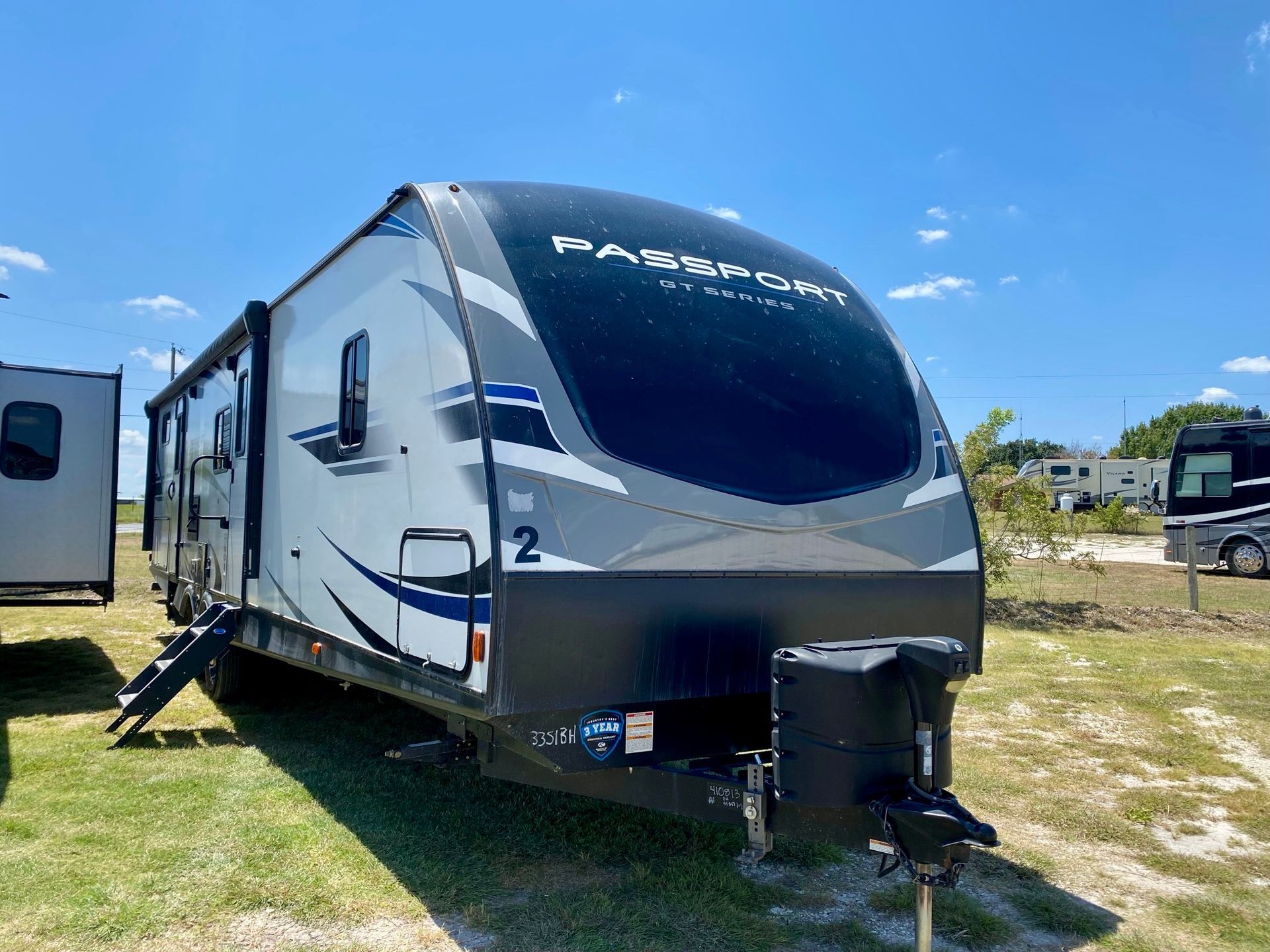 A white and black trailer is parked in a grassy field.