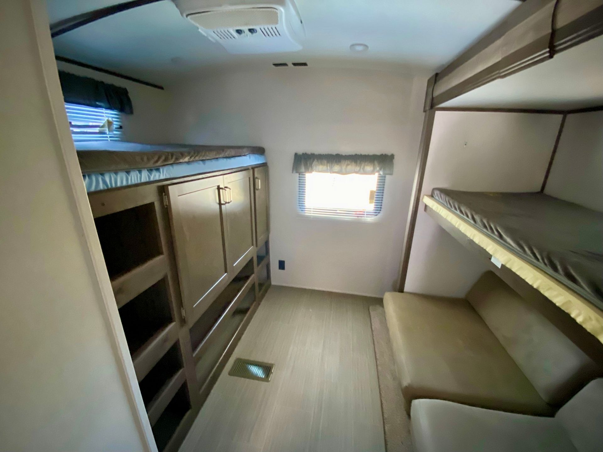 A small room with bunk beds , a couch , and a window.