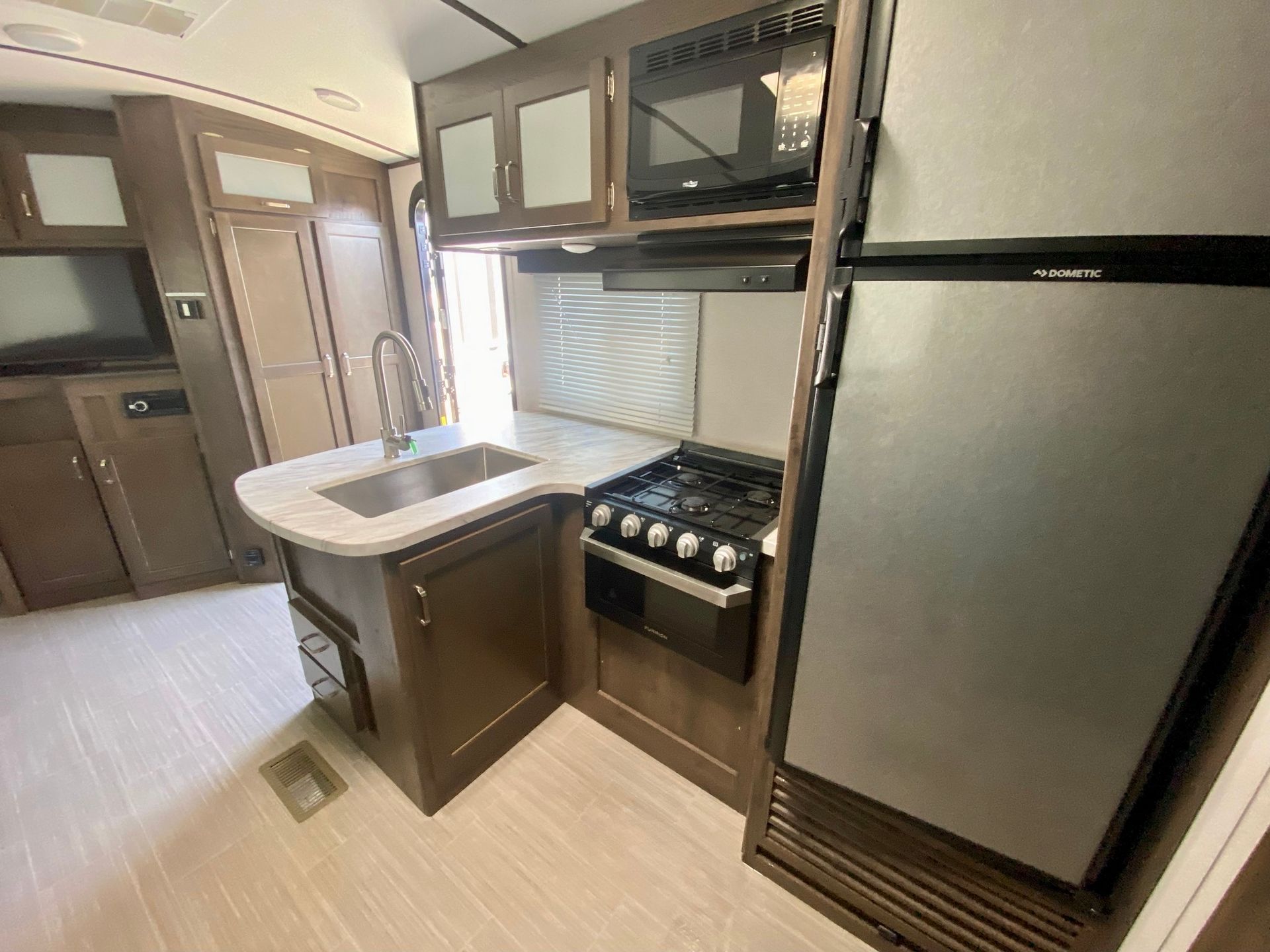 A kitchen in a rv with a sink , stove , refrigerator and microwave.
