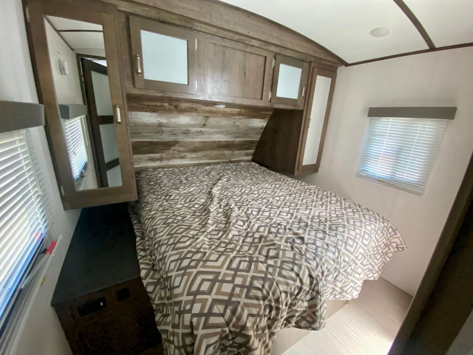 A bedroom in a trailer with a bed and a window.