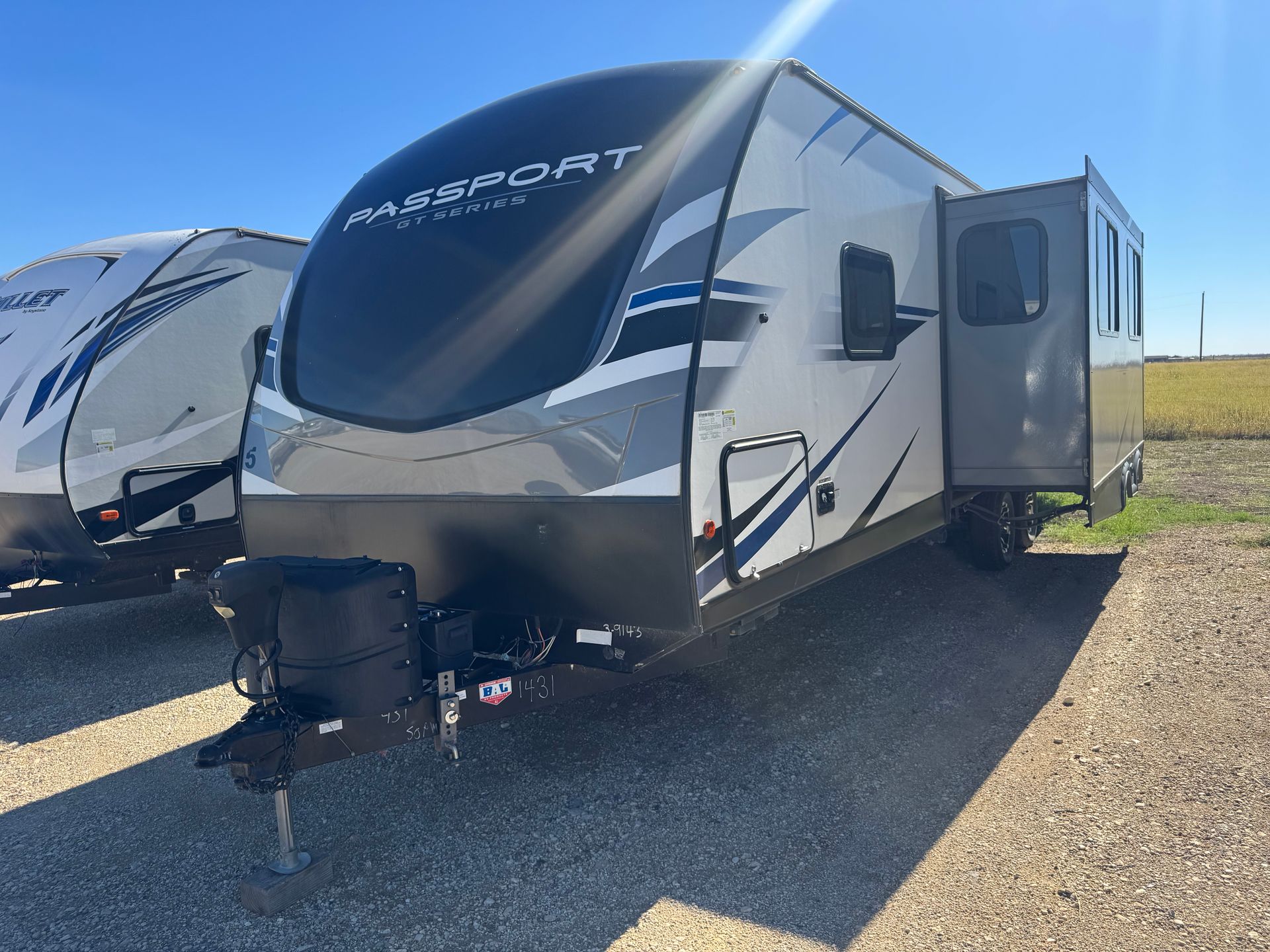 A white and black rv is parked in a gravel lot.