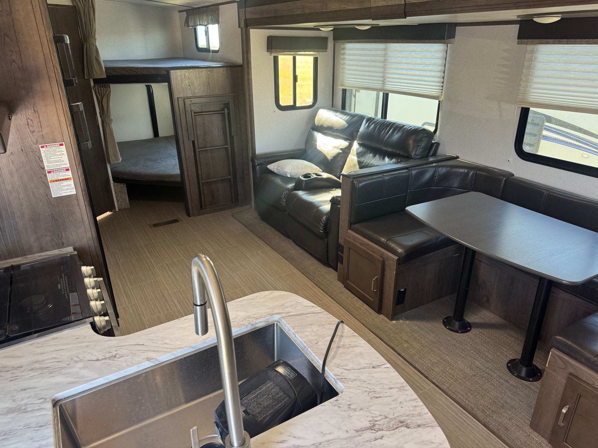 The inside of a rv with a sink , couch , table and bunk beds.