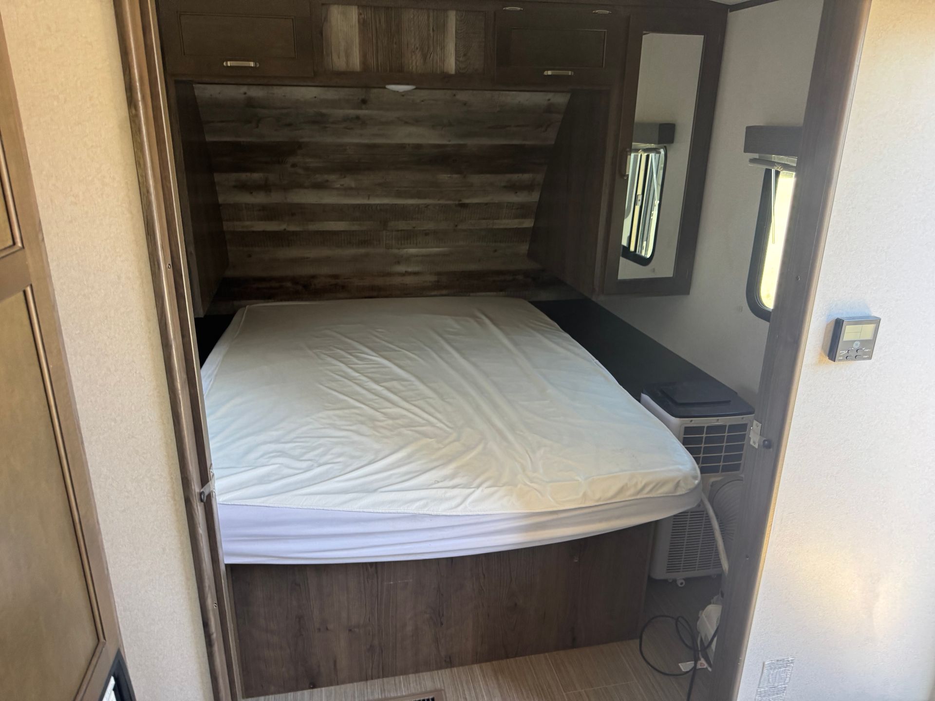 A bedroom in a trailer with a bed and a mirror.