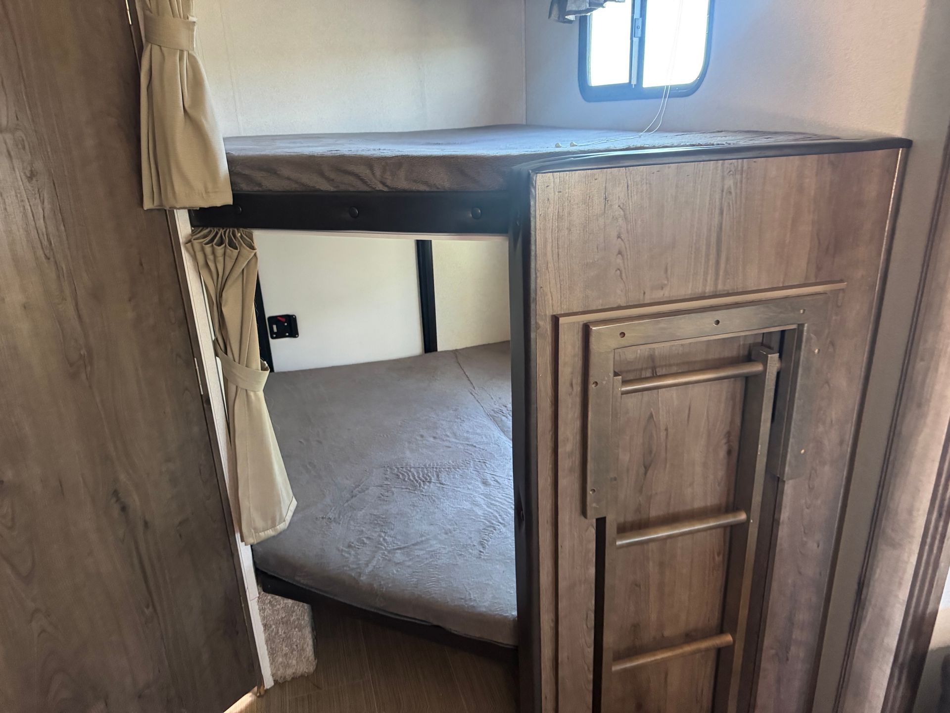 A bedroom in a rv with a bunk bed and a ladder.