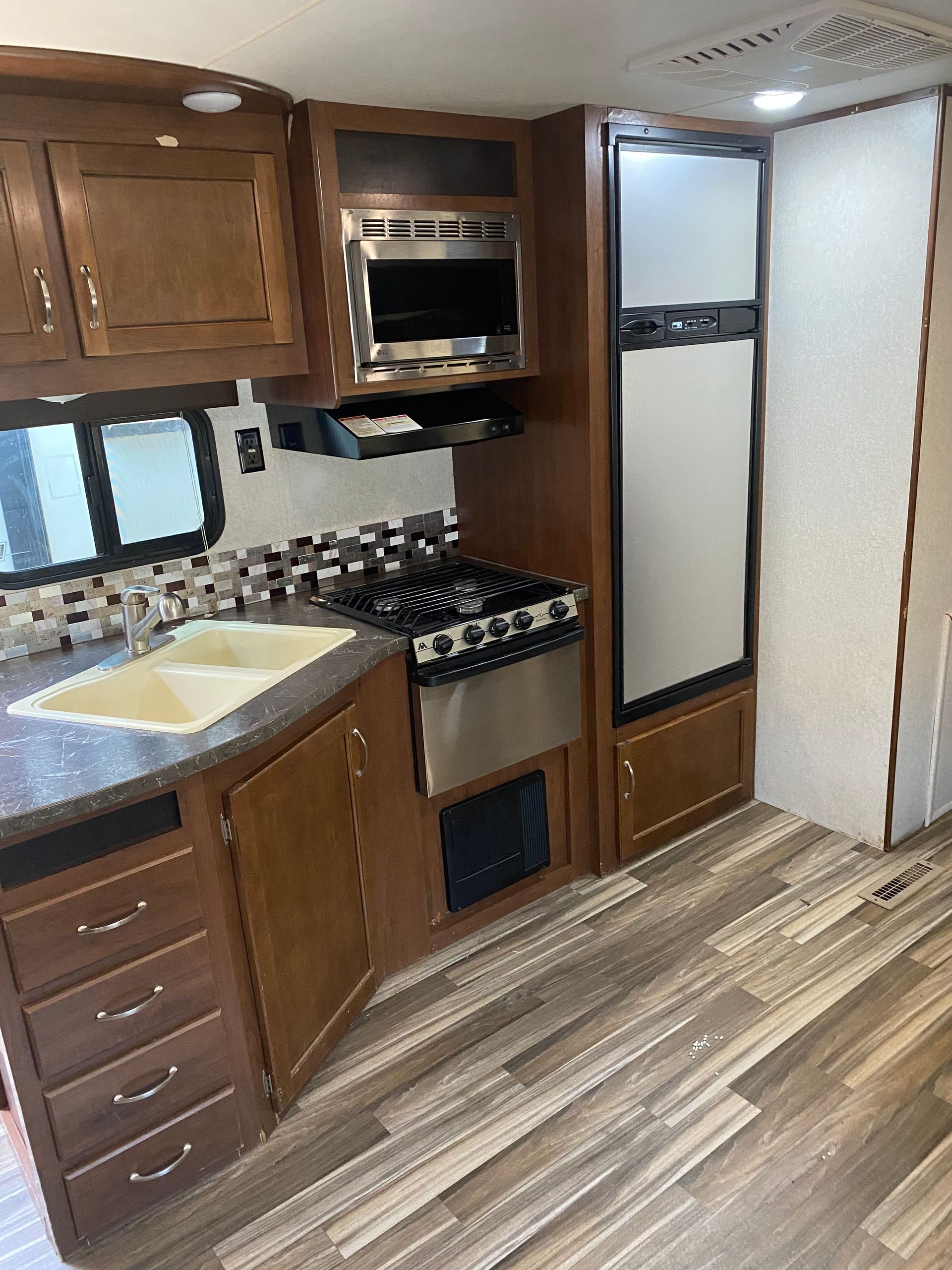 A kitchen in a rv with a sink , stove , refrigerator and microwave.