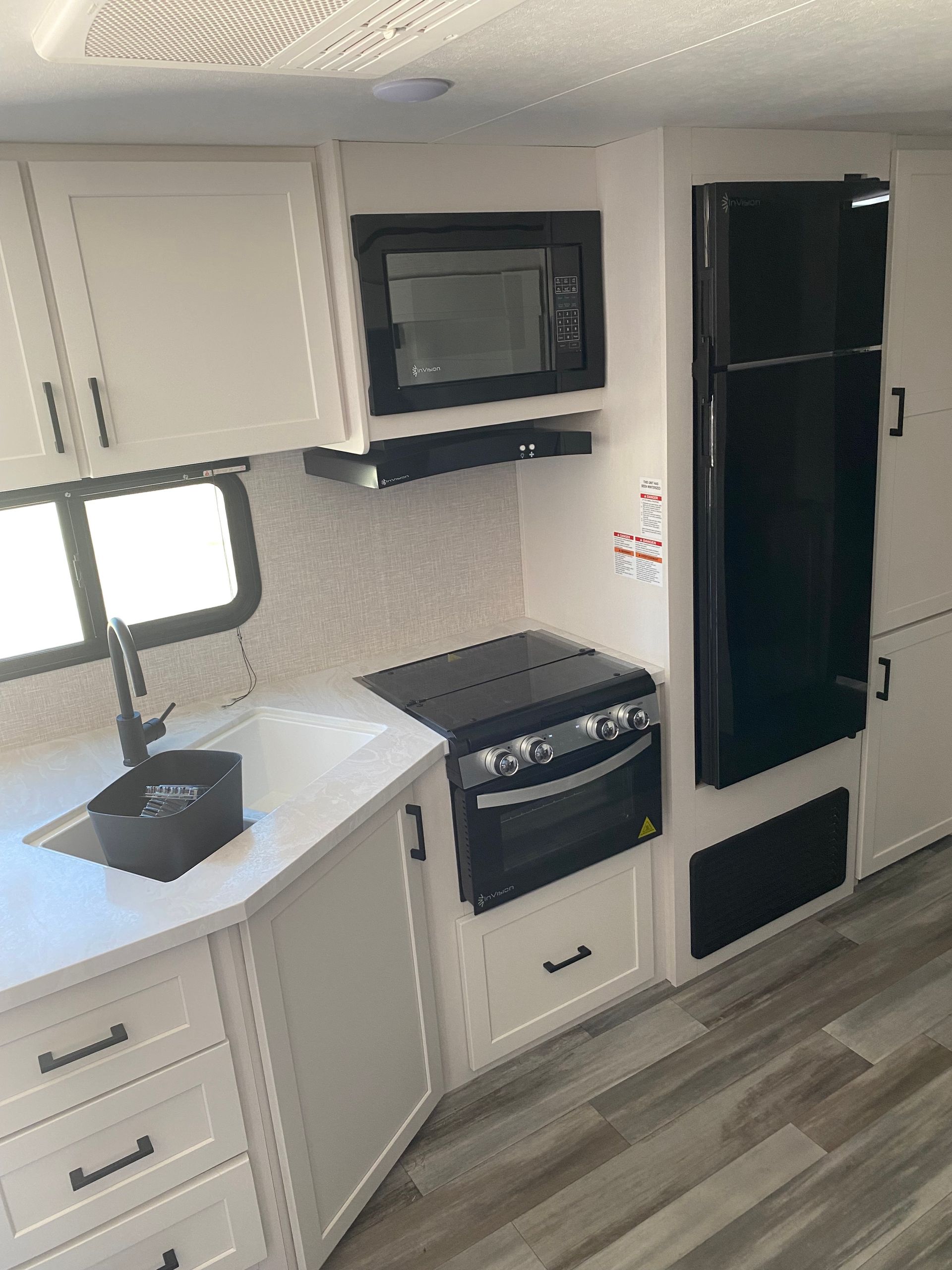 A kitchen in a trailer with a refrigerator , stove , microwave and sink.