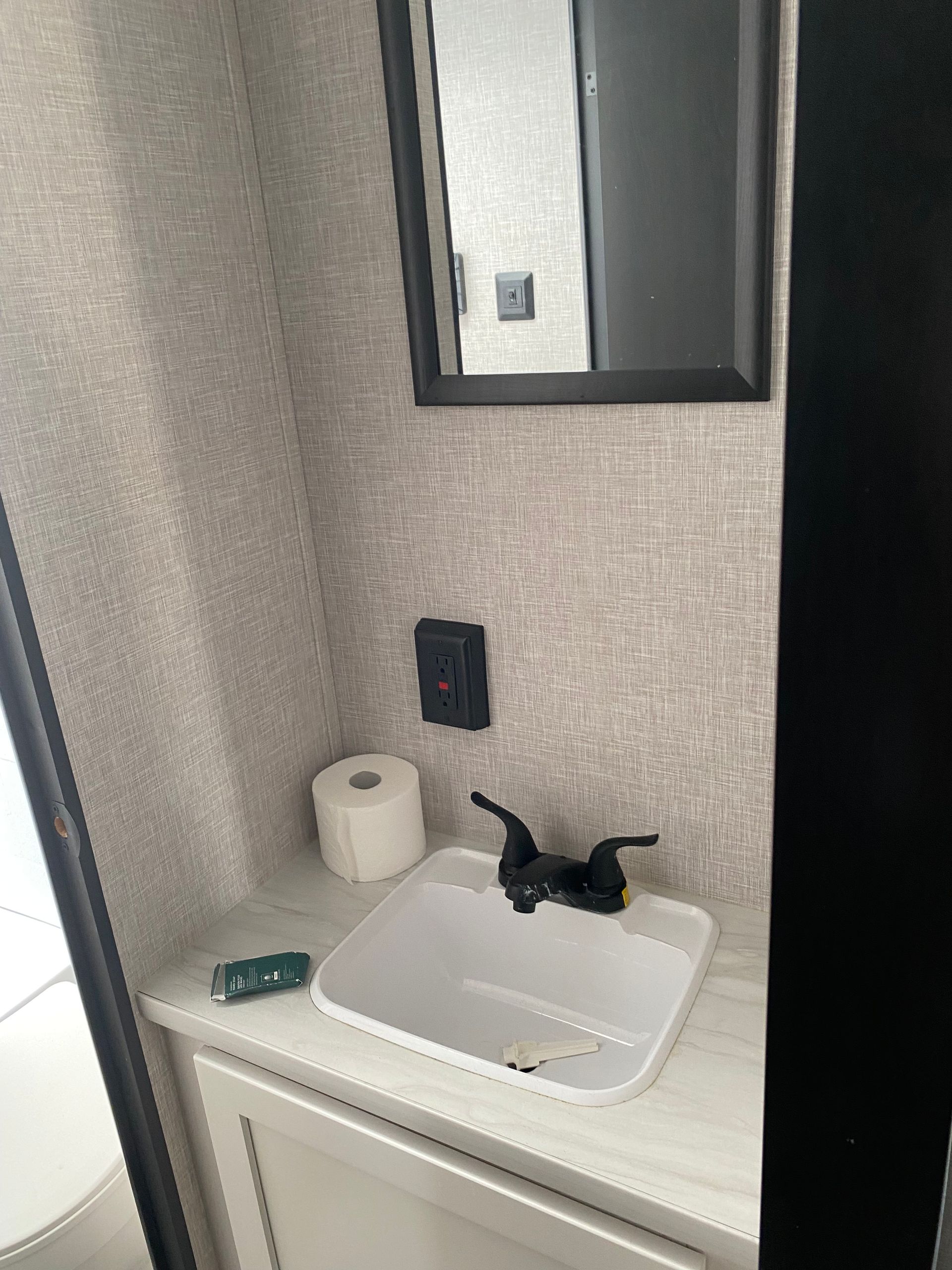 A bathroom with a sink , mirror and toilet paper.