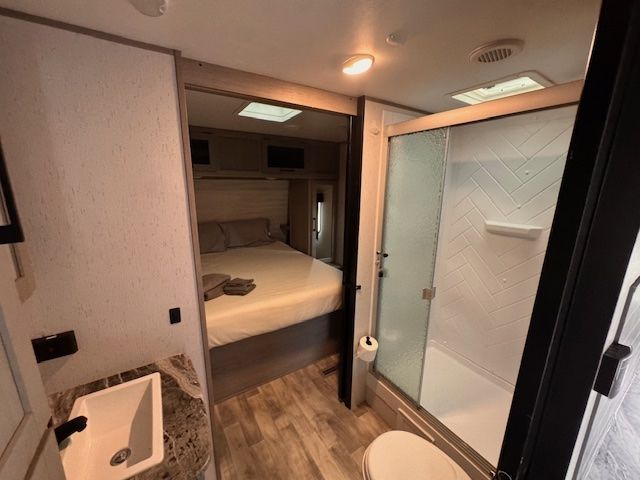 A bathroom with a toilet , sink , shower and bed.
