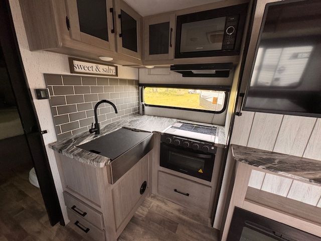A kitchen in a rv with a sink , stove , microwave and television.