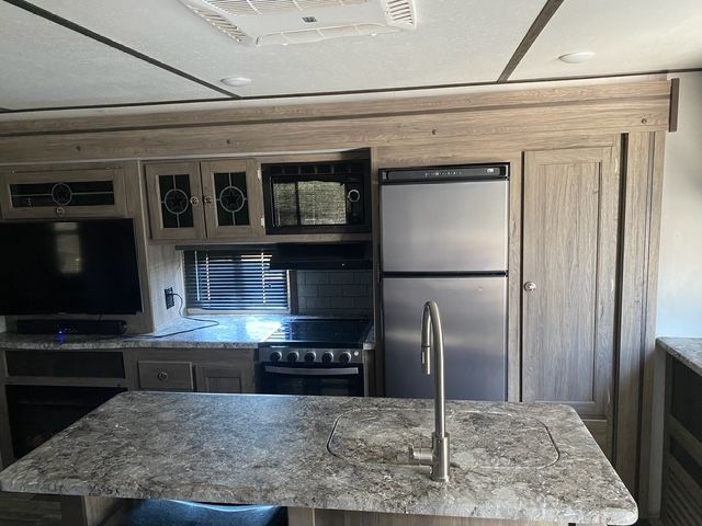A kitchen with a stove , refrigerator , sink and television.