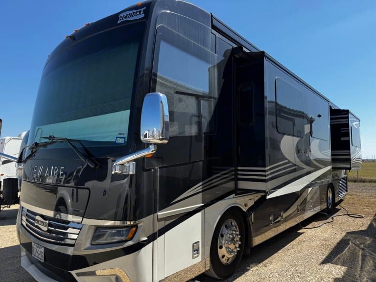 A large black and white rv is parked in a gravel lot.