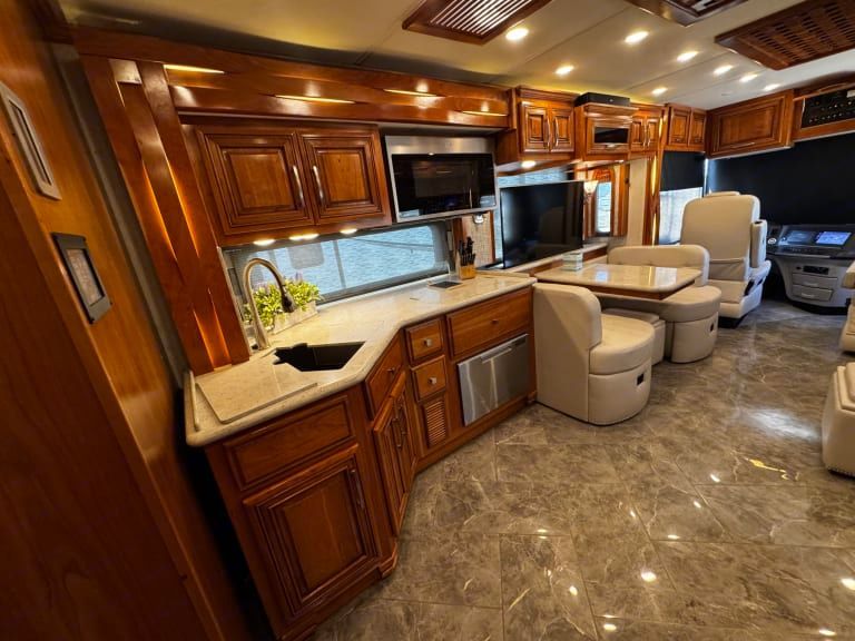 A kitchen in a rv with wooden cabinets , a sink , a table and chairs.