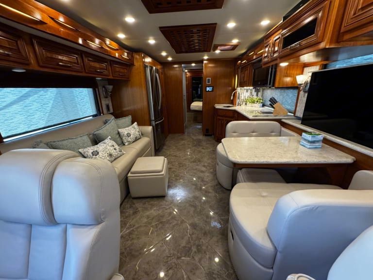 The inside of a rv with a couch , table and television.