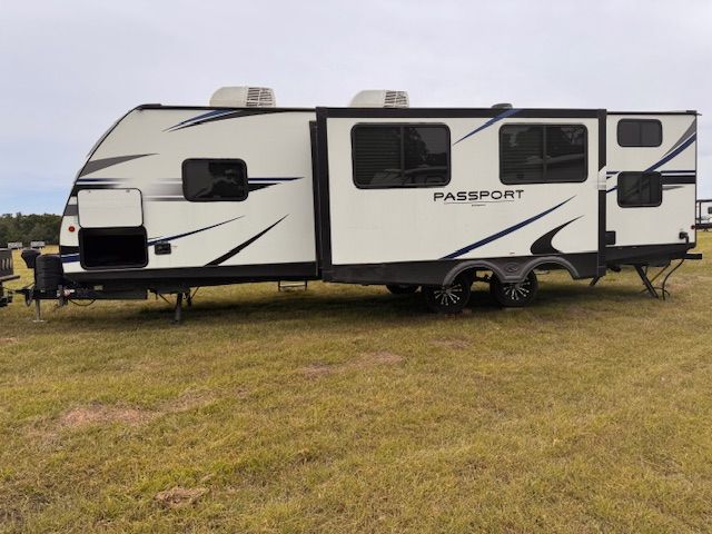 A white passport trailer is parked in a grassy field.