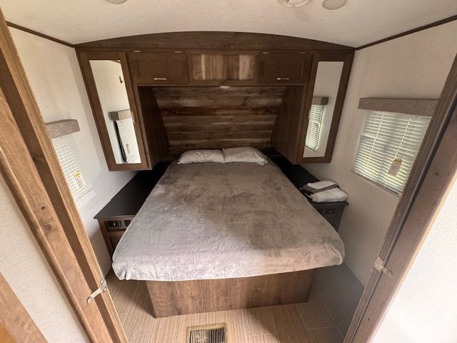 A bedroom in a trailer with a bed and mirrors.