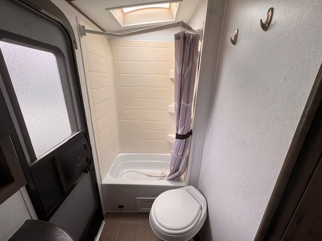 A bathroom with a toilet , shower and window