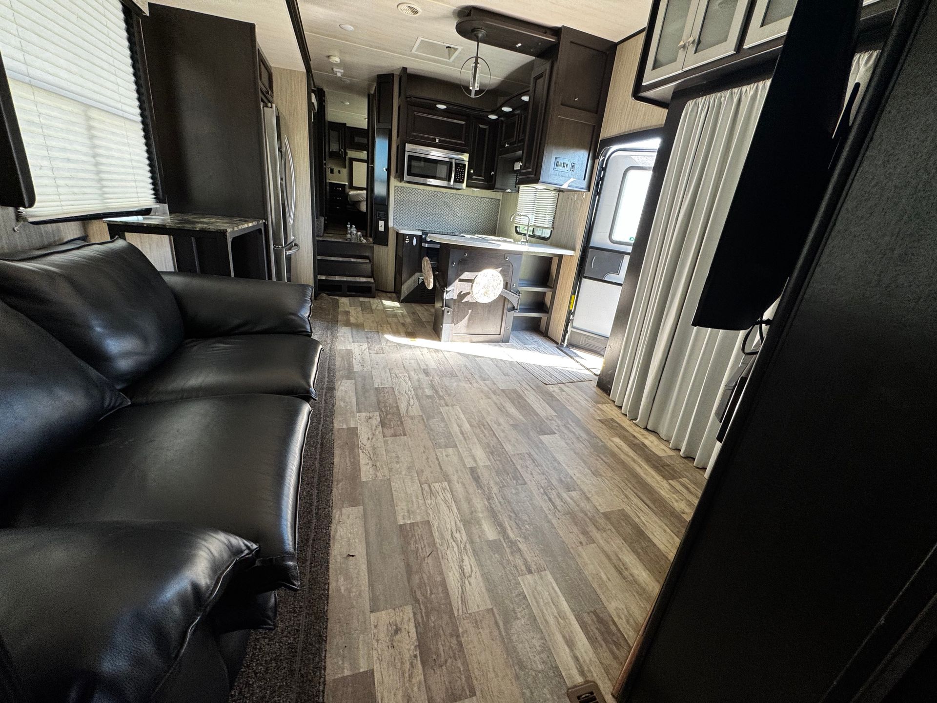 A living room in a rv with a black couch and wooden floors.