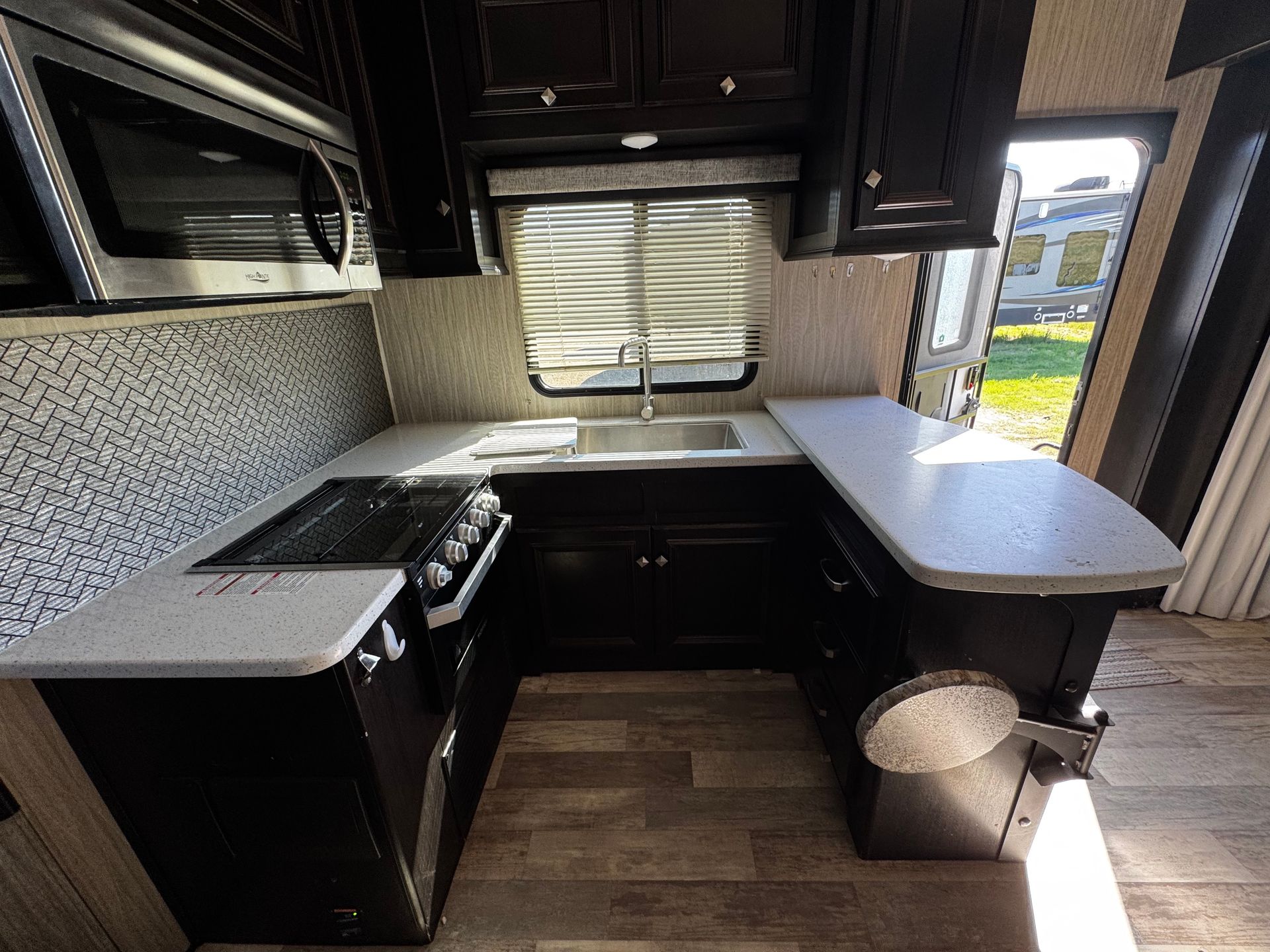 A kitchen with black cabinets , a stove , a sink , and a microwave.