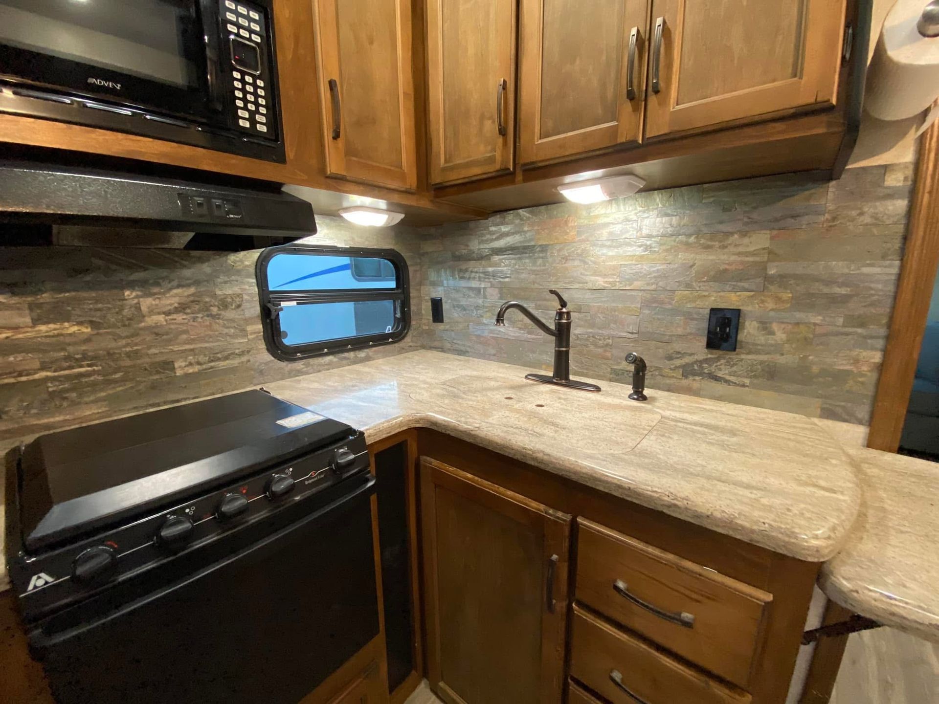 A kitchen in a trailer with a stove , sink , microwave , and cabinets.