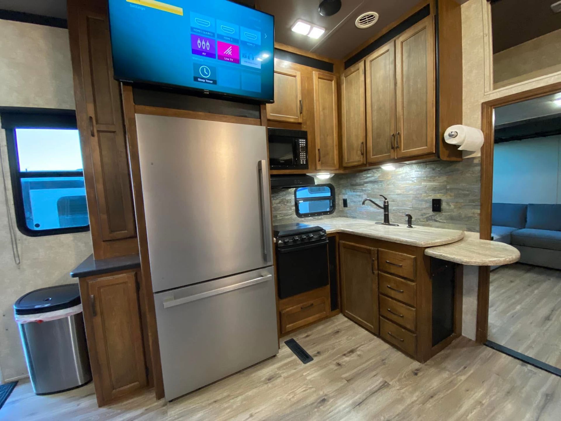 A kitchen in a rv with stainless steel appliances and a flat screen tv.