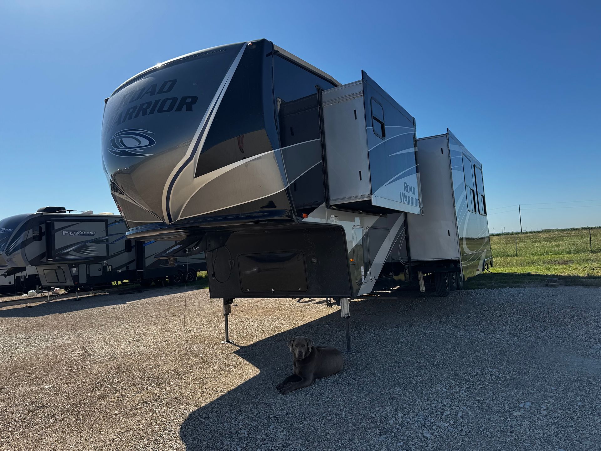 A rv is parked in a gravel lot in a field.