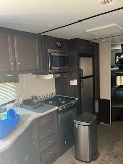 A kitchen in a rv with a stove , refrigerator , microwave , sink and trash can.