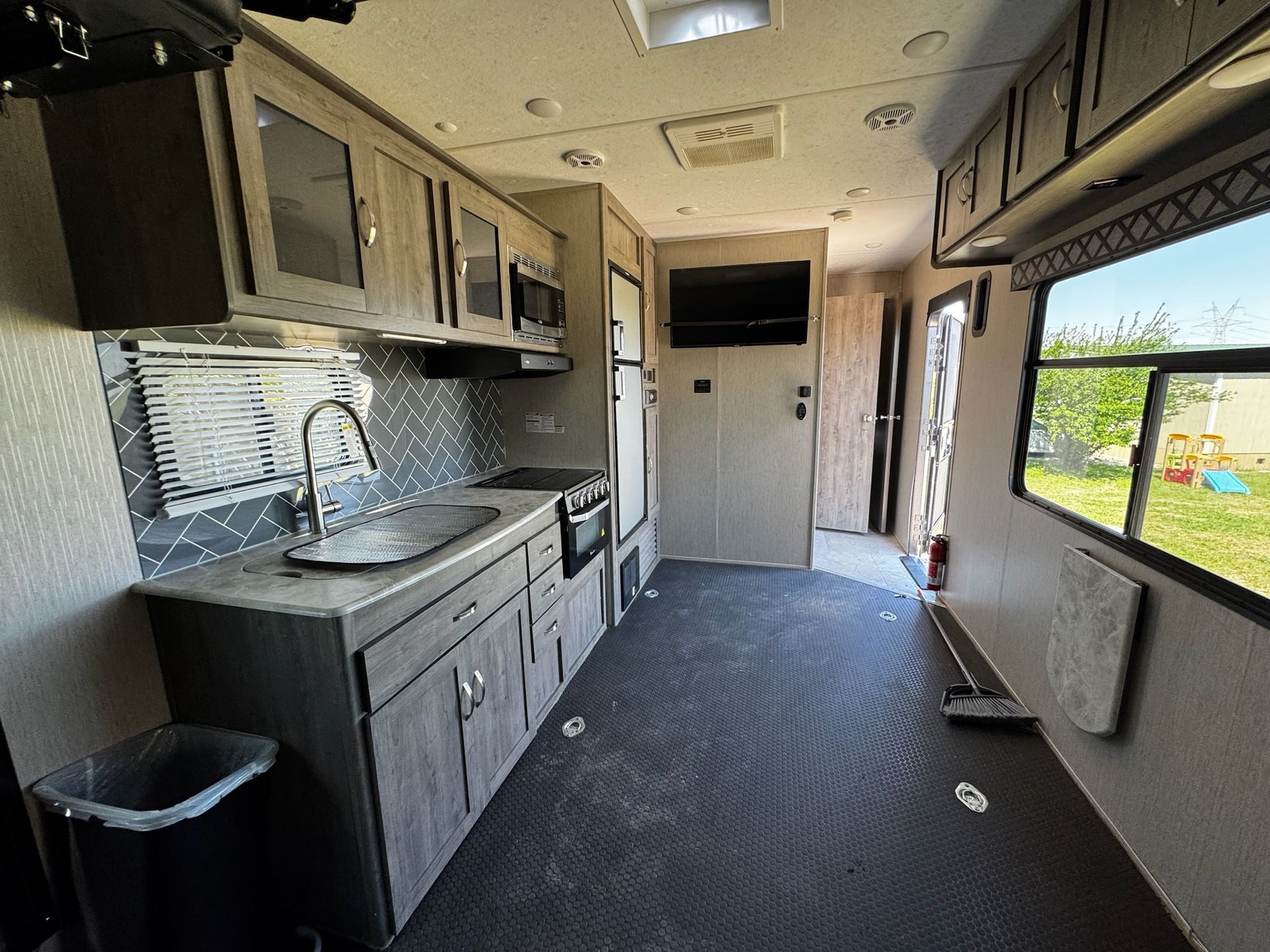 A kitchen in a trailer with a sink , stove , refrigerator and television.