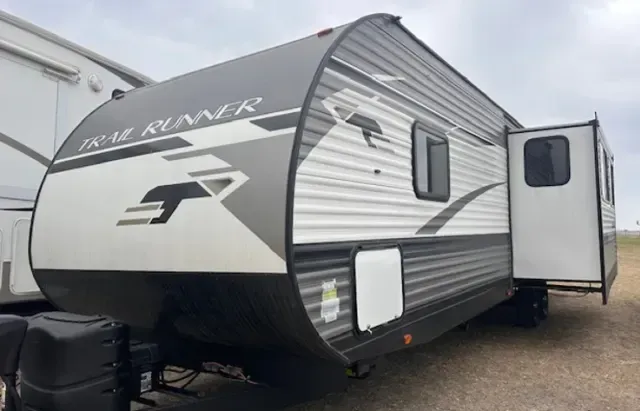 A white and black trailer is parked in a field.