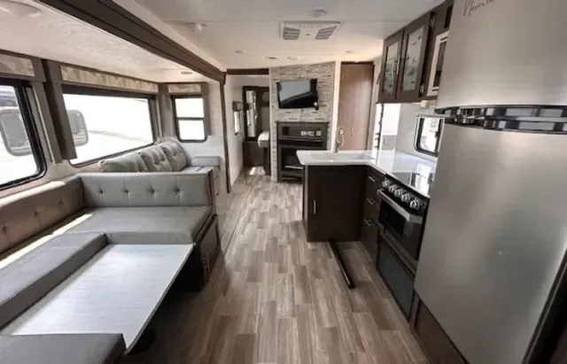 The inside of a rv with a couch , stove , refrigerator , and television.