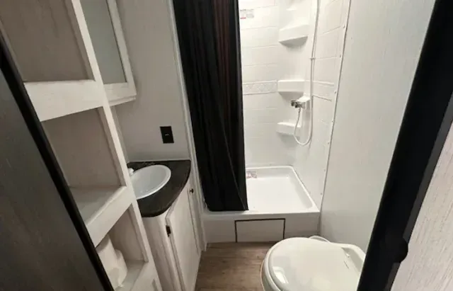 A bathroom in a trailer with a toilet , sink and shower.