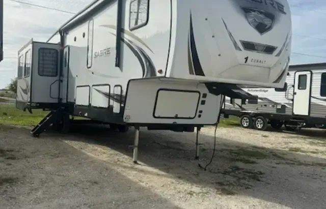 A white rv is parked in a dirt lot next to other rvs.