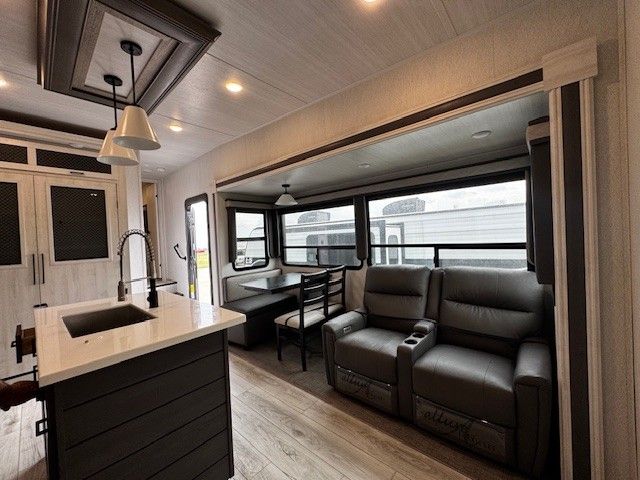 A living room in a rv with a sink , chairs , and a table.