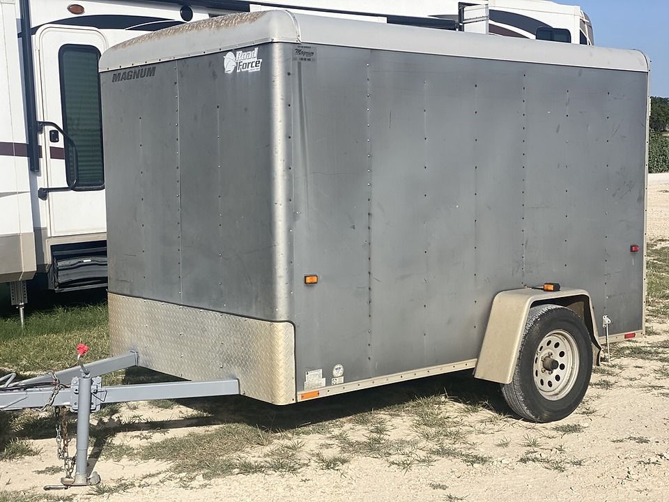 A gray trailer is parked in a dirt lot next to a rv.