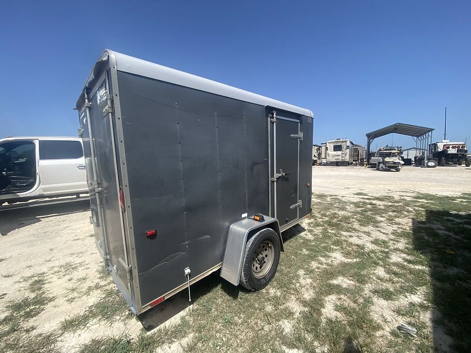 A small trailer is parked in a dirt field next to a truck.