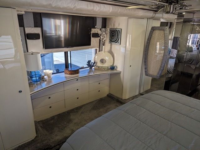 A bedroom in a rv with a bed , dresser , television and ceiling fan.
