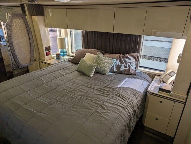 A bed with a gray comforter and pillows in a room with a window.