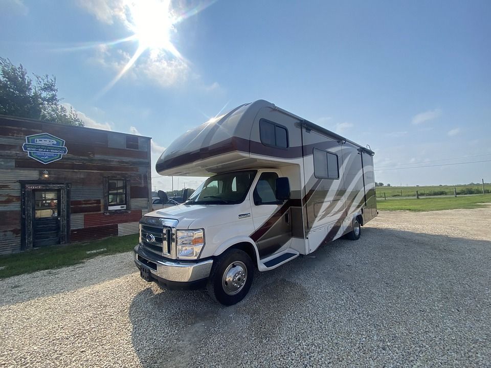 A white rv is parked in a gravel lot in front of a building.