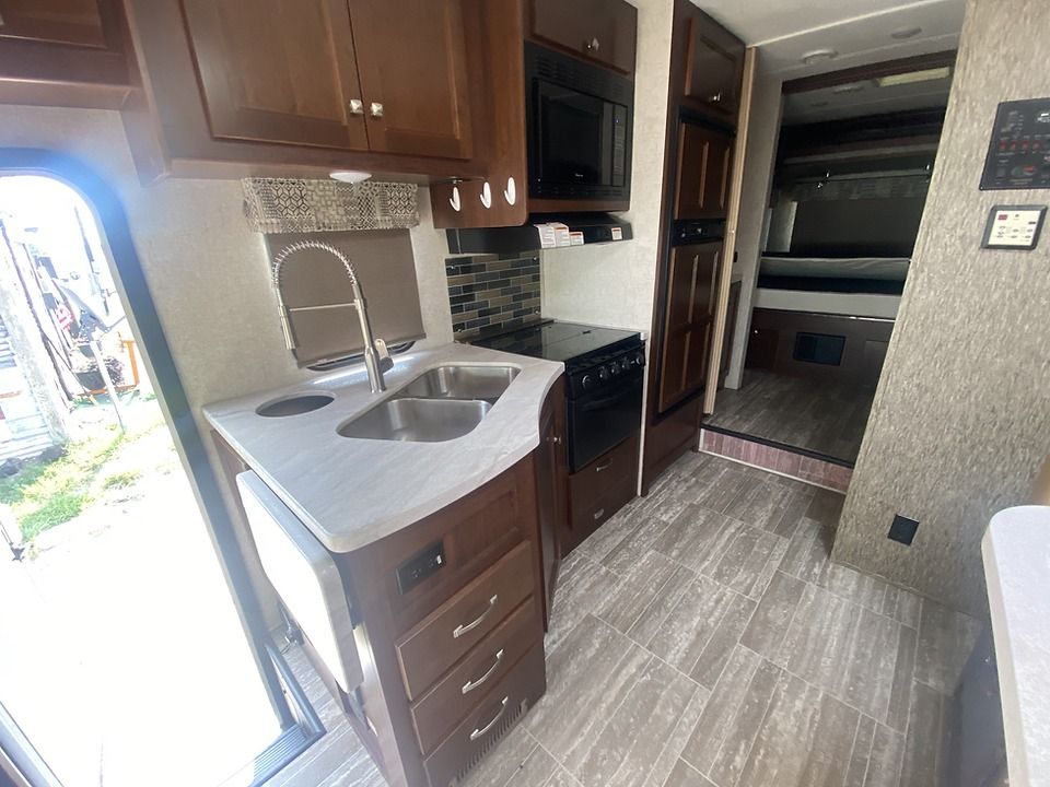 A kitchen in a rv with a sink , stove and microwave.