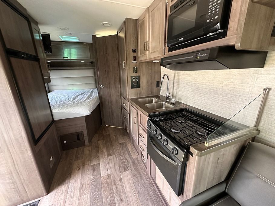 A kitchen in a rv with a stove , sink , and microwave.