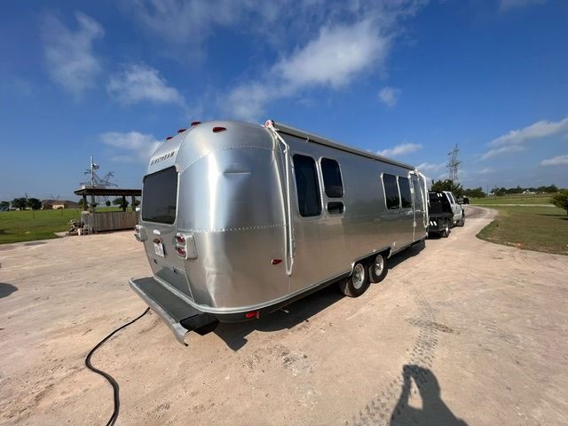 A silver airstream trailer is parked on a dirt road