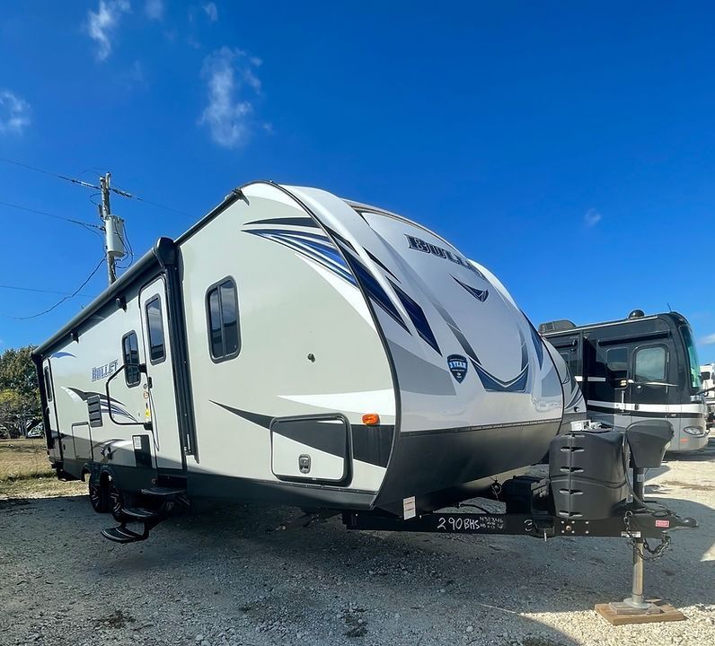 A white and black trailer is parked in a gravel lot.