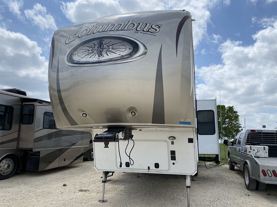 A silver rv is parked in a gravel lot next to a truck.