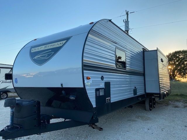 A small trailer is parked in a gravel lot.