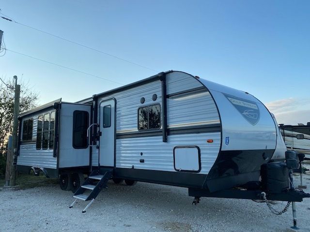 A silver and black trailer is parked in a gravel lot.