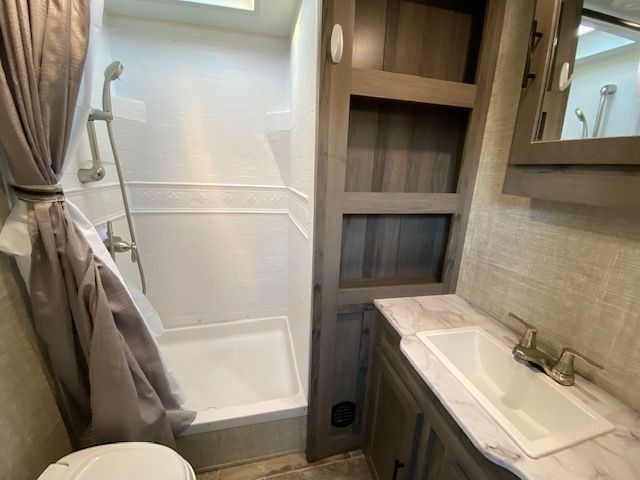 A bathroom with a toilet , sink , shower and mirror.
